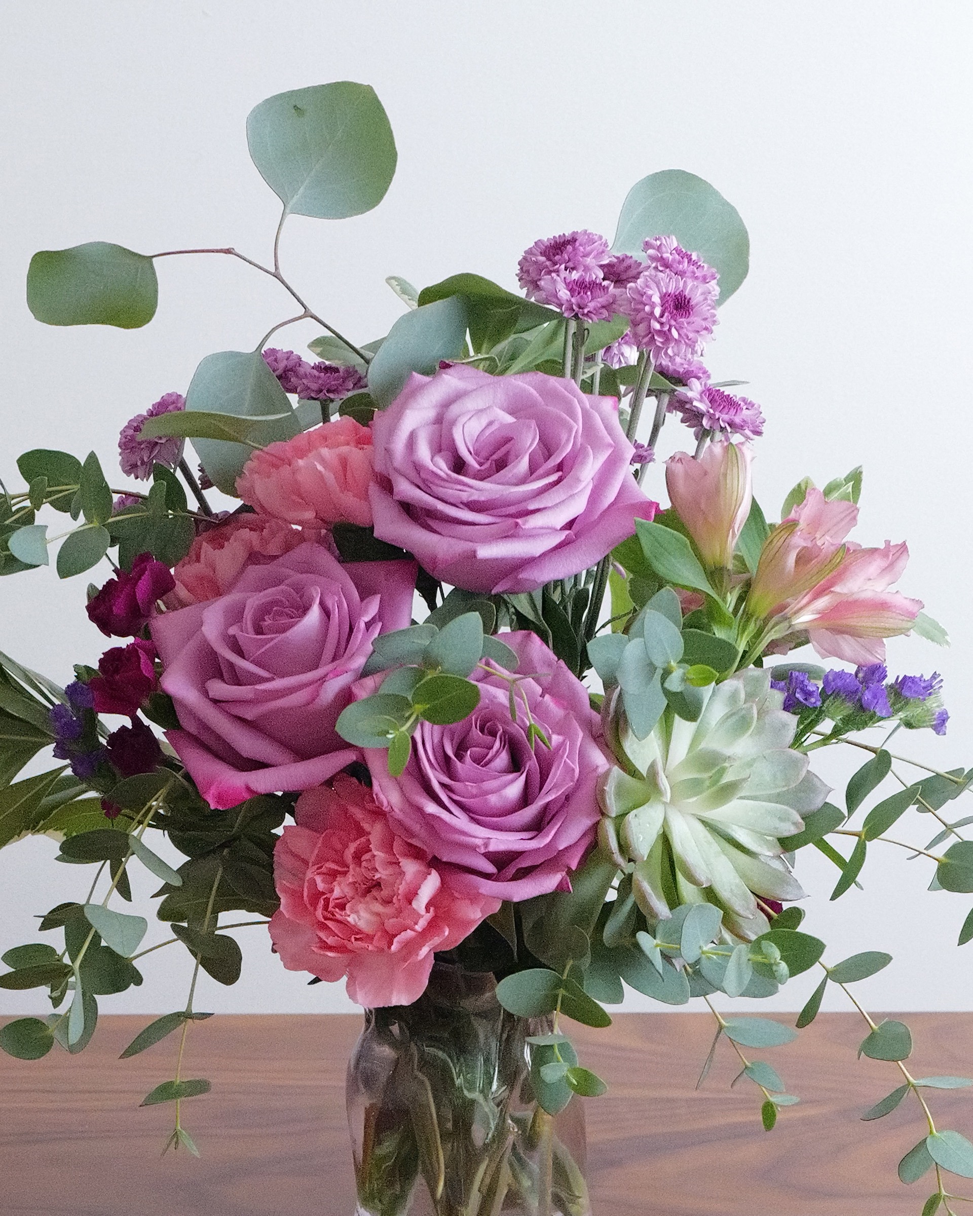 Close view of lavender roses, coral carnations, pink alstroemeria and a pale green echeveria among eucalyptus