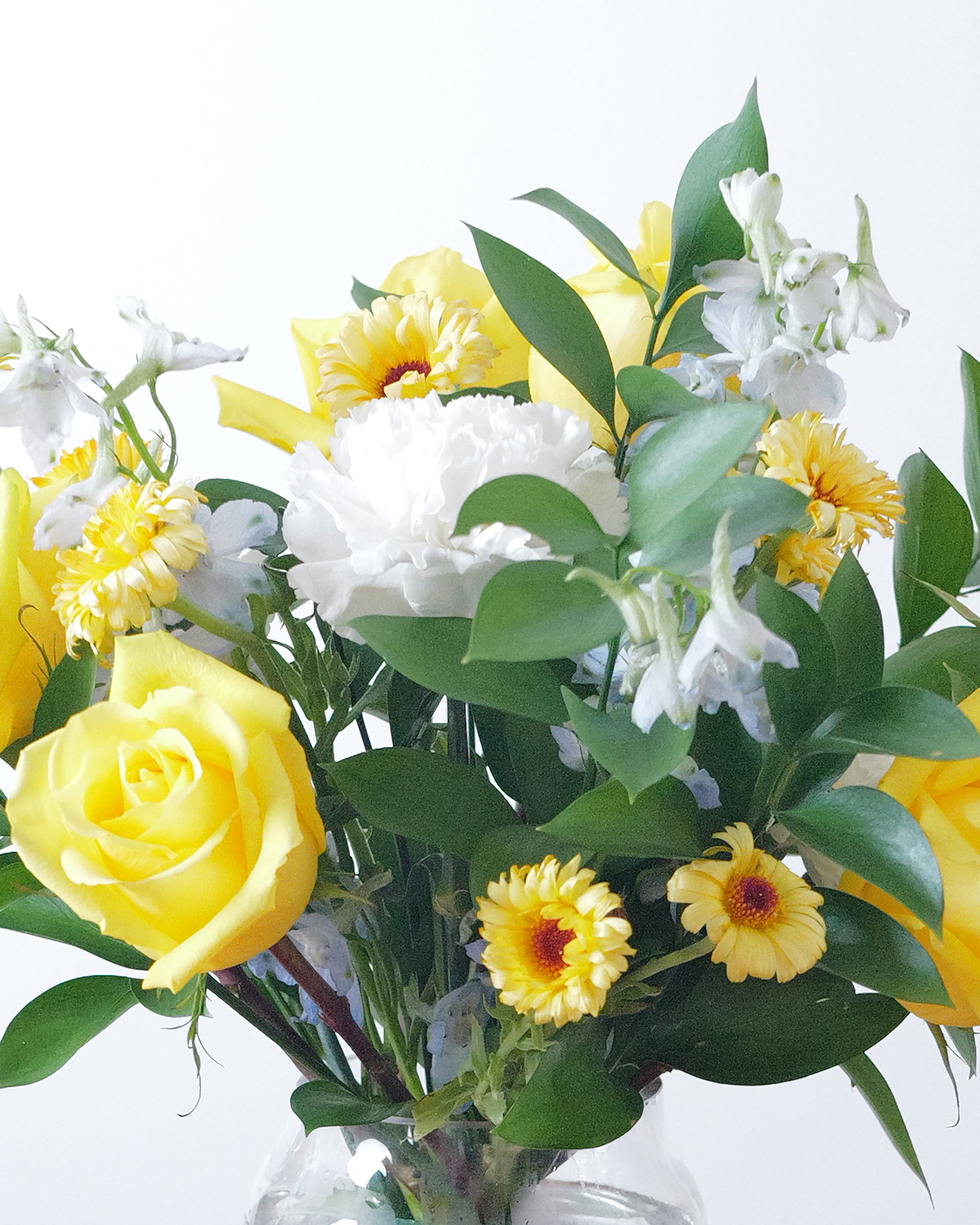 Close view of yellow roses, a ruffled white carnation, golden blooms with dark centers and pale blue-white flowers among