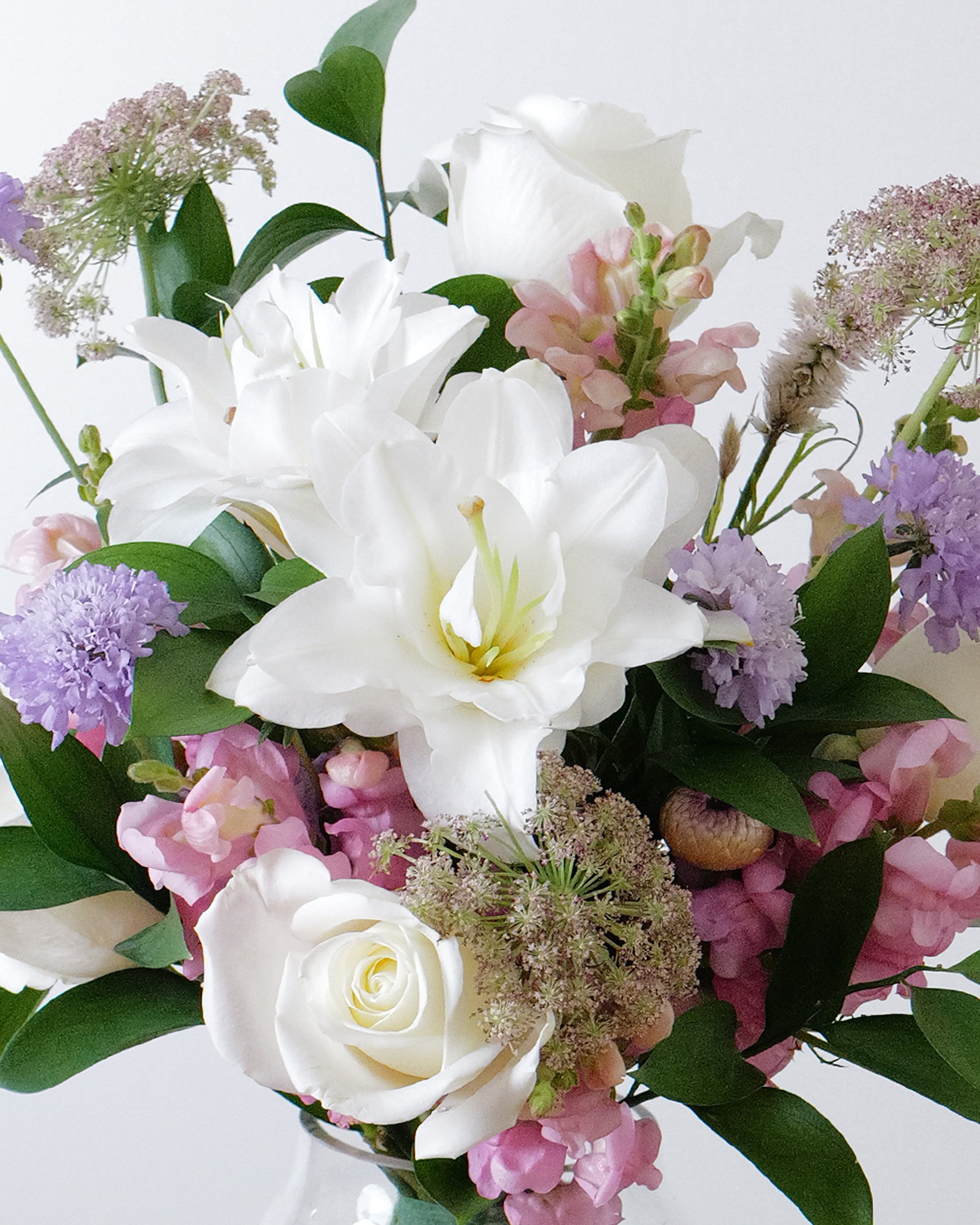 Close view of white lilies and a white rose among pink snapdragons, lavender blooms and lacy filler