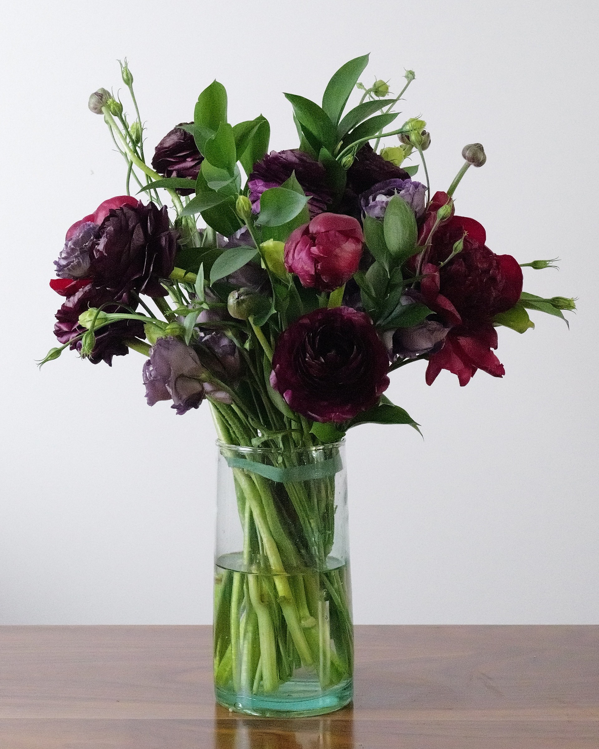 Burgundy, wine, dark and purple with green leaves in a clear glass vase on a wood table