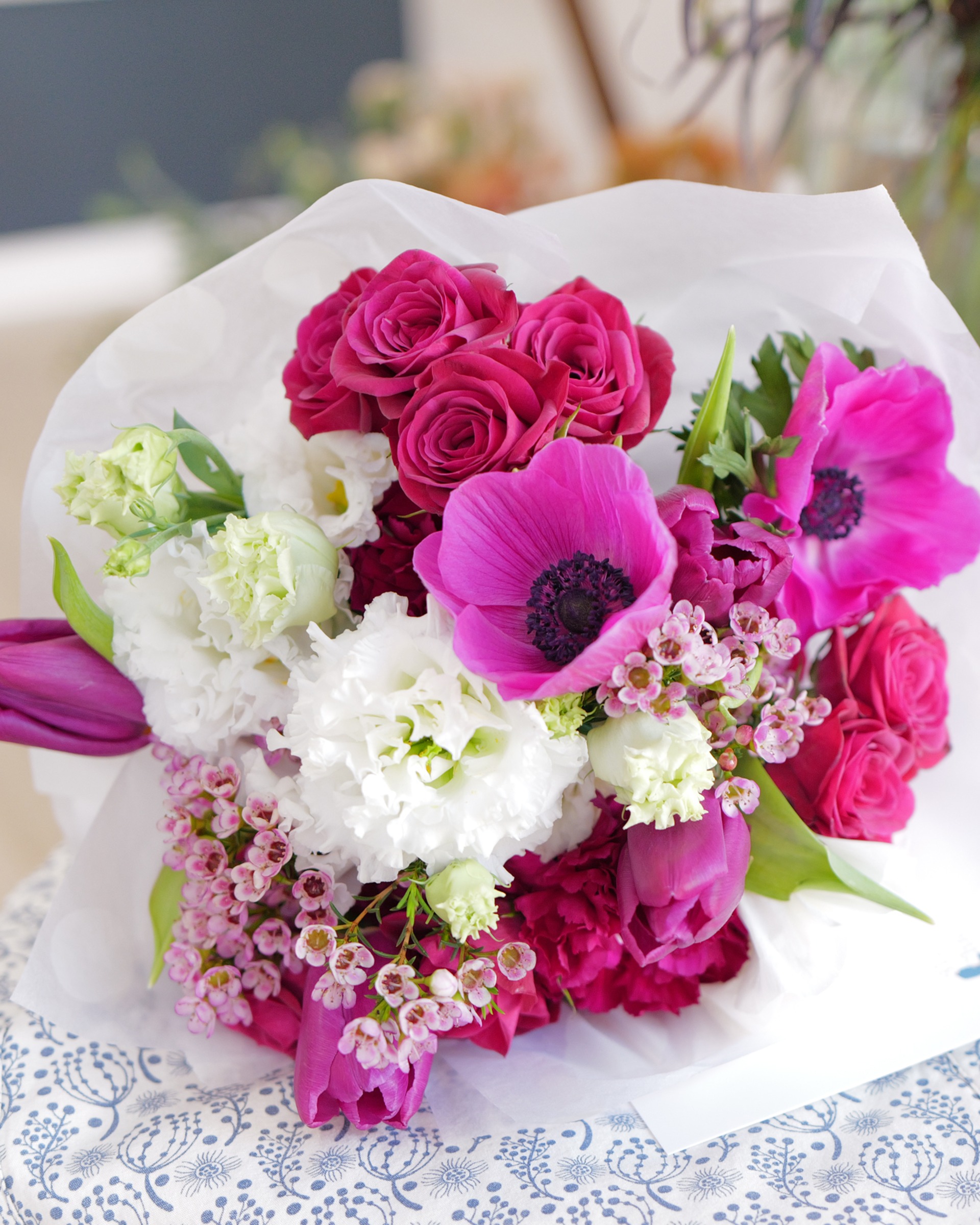Magenta anemones, deep pink roses, purple tulips, white lisianthus and blush wax flower wrapped in white paper