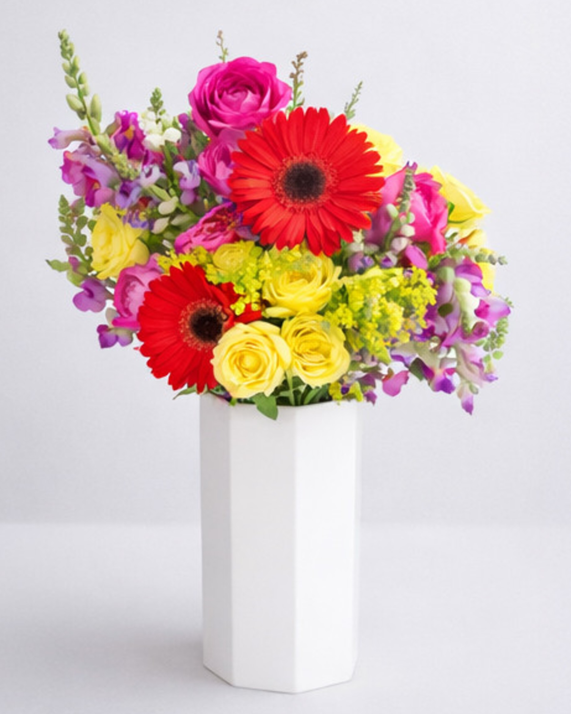 Red gerberas, hot pink and yellow roses with purple snapdragons and yellow solidago in a white faceted vase
