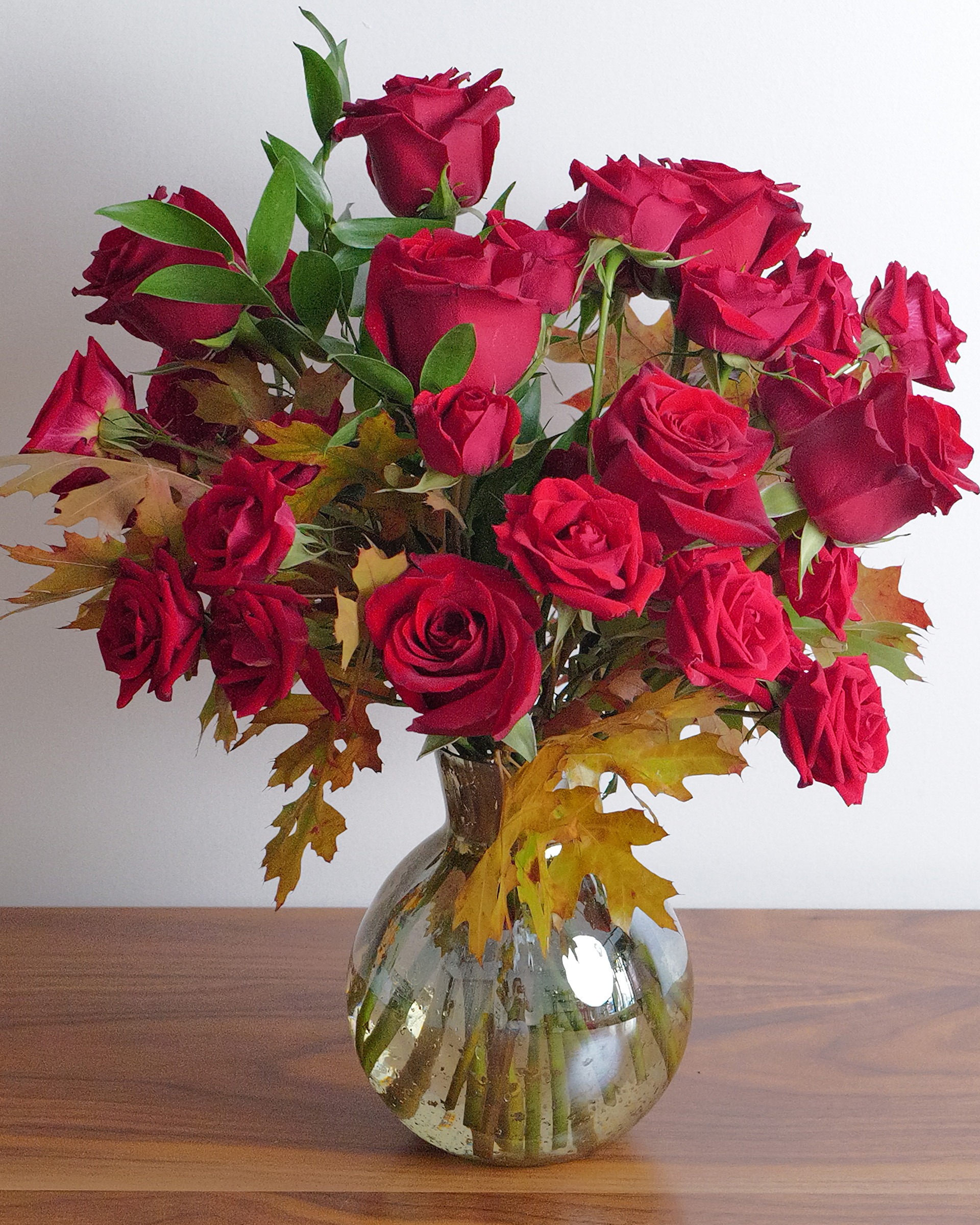 Fall into Romance, a fall anniversary arrangement of red roses and autumn leaves in glass, seen from slightly above