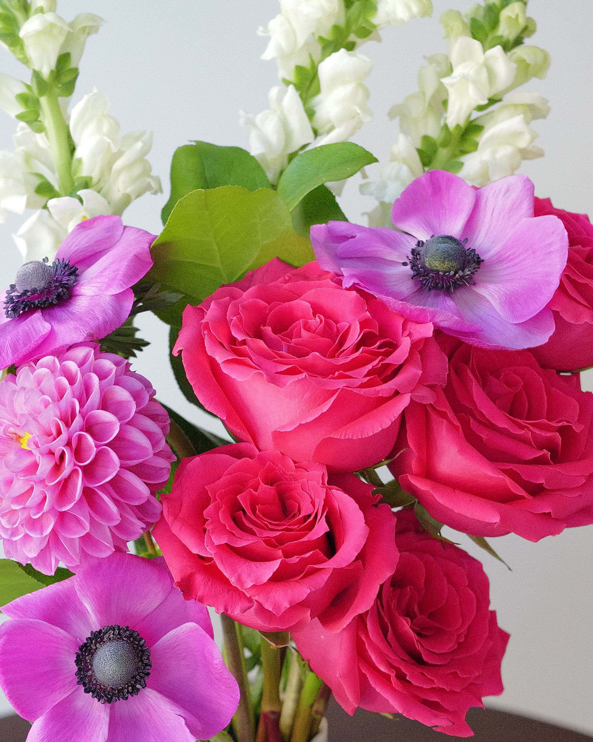 Close view of hot pink roses, magenta anemones with dark centers, a pink dahlia and white snapdragons